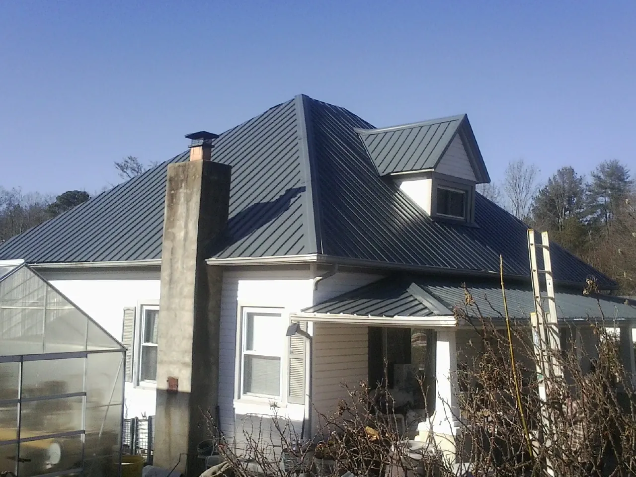 Dark blue standing seam metal roof on a white farmhouse with dormer — Slate & Tile Roof Repair by Roofing Brothers in Noti