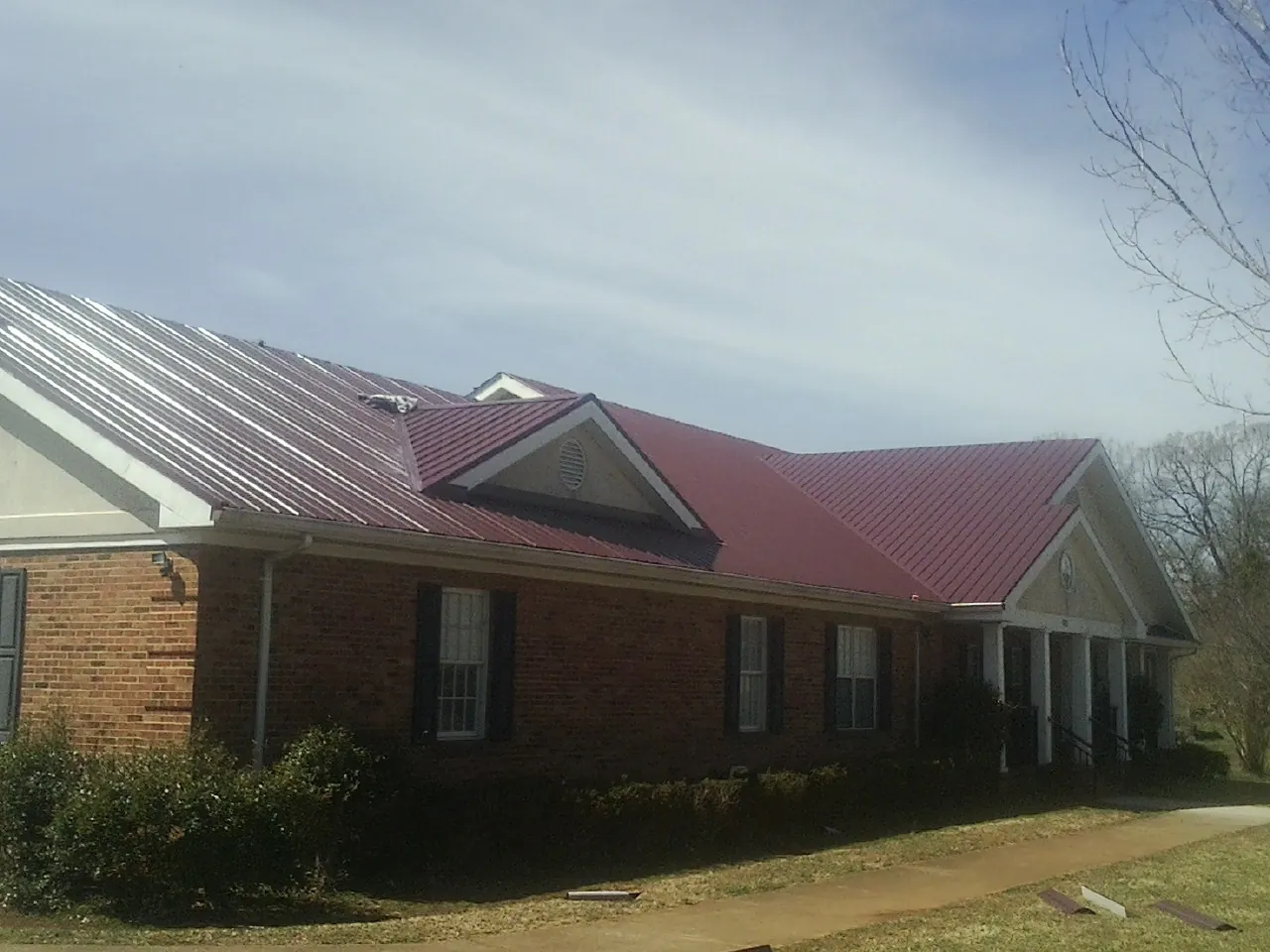 Red metal roof with gabled entries on a long brick building, from a Hail Damage Roof Repair job in Noti