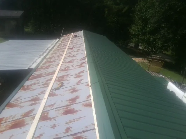 Old rusted panels beside newly installed green metal roofing — Wind Damage Roof Repair by Roofing Brothers in Noti