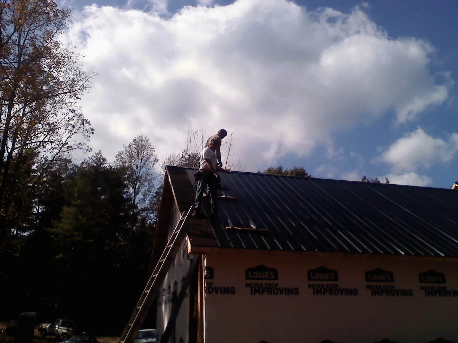 Roofer fastening dark metal panels high against a cloudy sky, from a Roof Inspection job in Noti