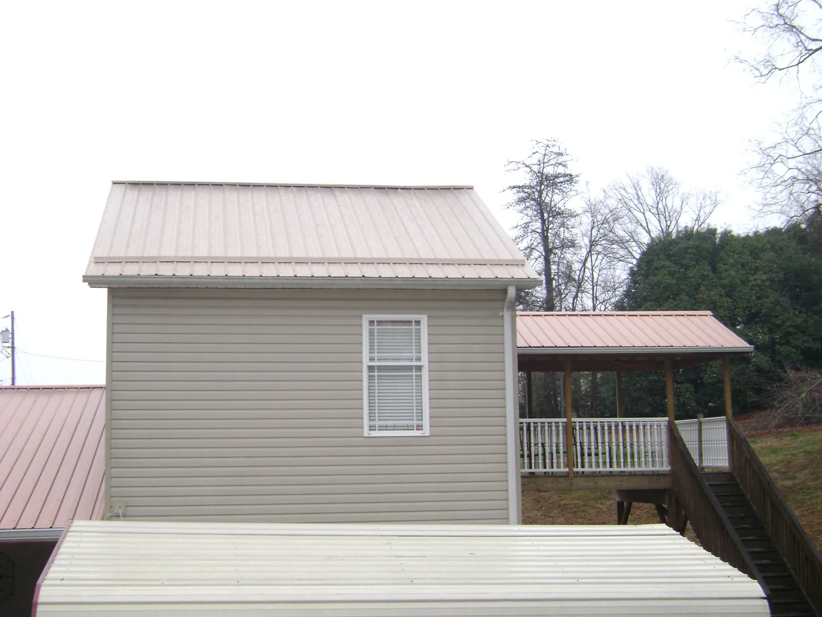 Tan metal roofs on a two story addition and attached porch, from a Roof Replacement job in Noti